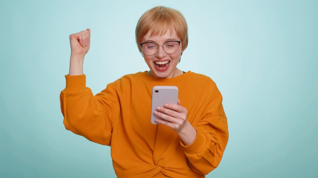 スマートフォンを見て歓喜する女性の画像